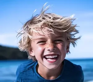 Portrait d'un garçon riant aux éclats, cheveux au vent. Une photo de vacances lumineuse symbolisant la joie de vivre et le bonheur en bord de mer.