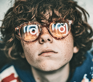 Portrait d'un adolescent au visage éclairé par la lueur bleutée d'un écran dans l'obscurité, symbolisant l'usage des réseaux sociaux et la dépendance au numérique.