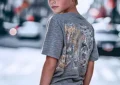 Adolescent blond en t-shirt gris imprimé et jean délavé, style streetwear urbain décontracté, arrière-plan ville floue